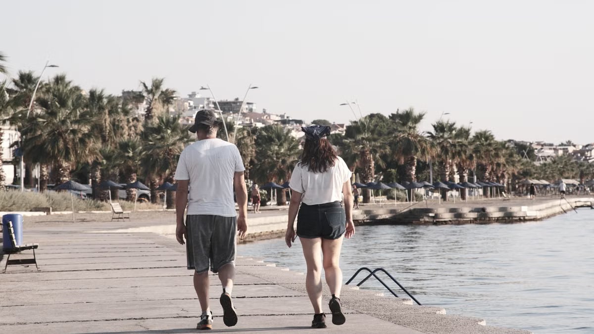 A couple enjoys a walk along the palm-lined waterfront of Foça, İzmir, Türkiye.